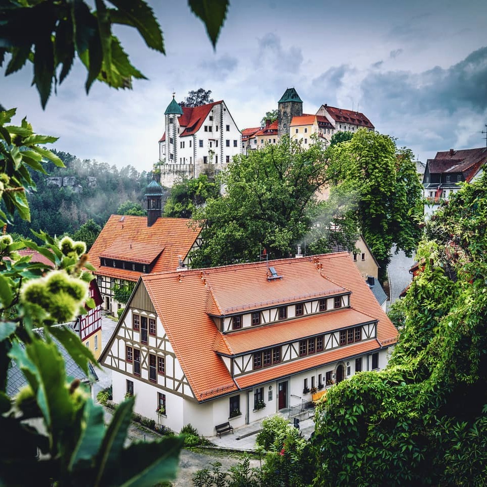 Fachwerkhäuser mit roten Ziegeldächern im Ort Hohnstein, darüber die Burg auf dem Felsen