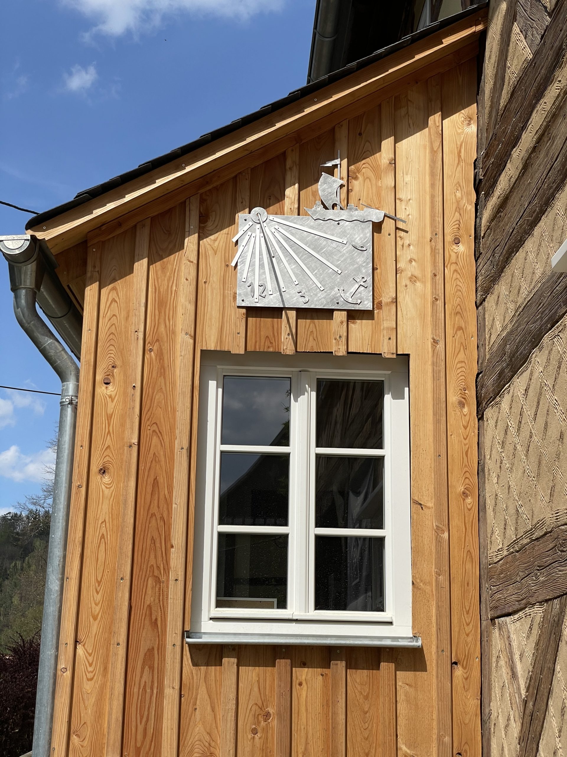 Sonnenuhr aus Metall an der holzverschalten Giebelwand des Umgebindehauses