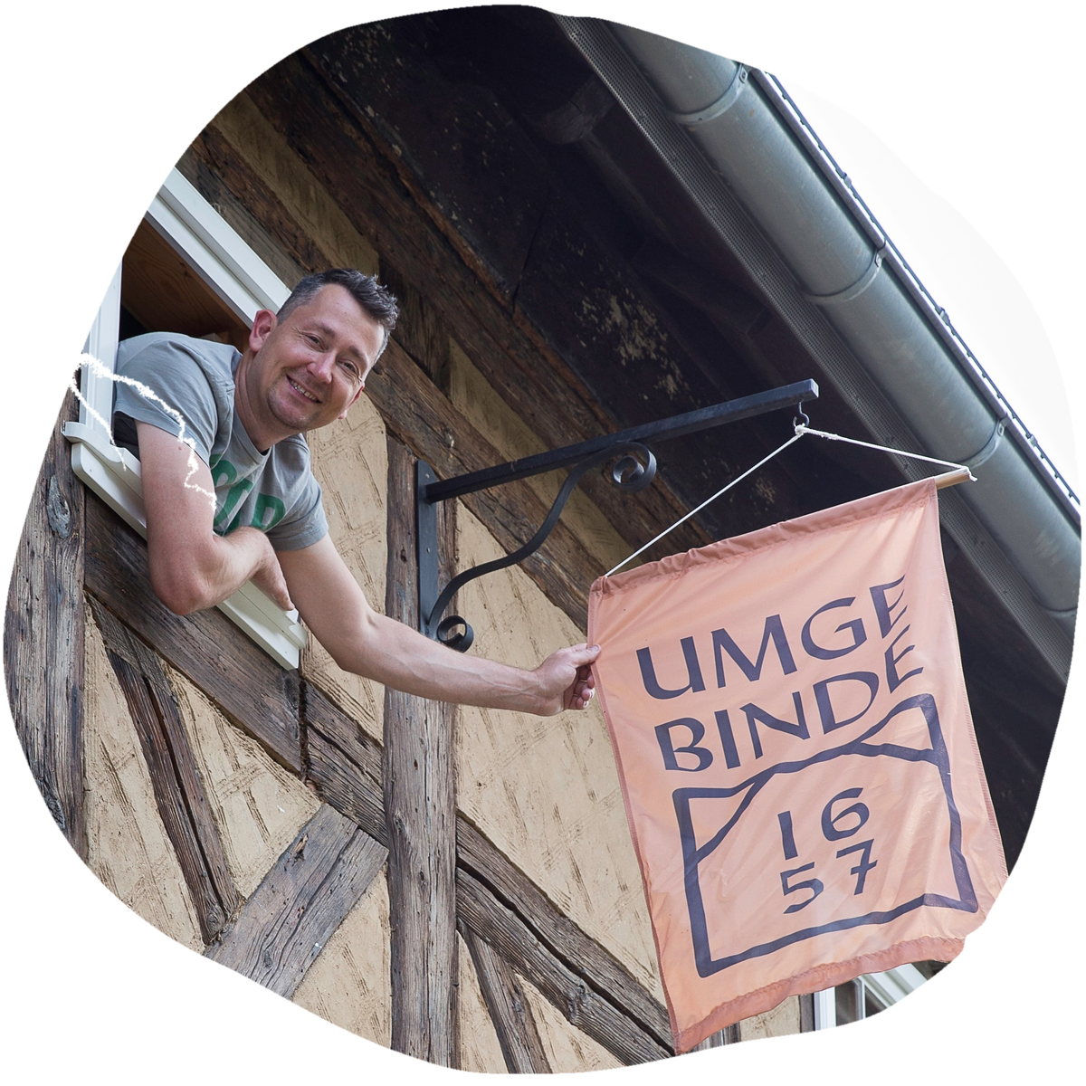 Felix Zschoge lehnt aus dem Fenster des Umgebindehauses und h&auml;ngt die Fahne mit dem Hauszeichen auf